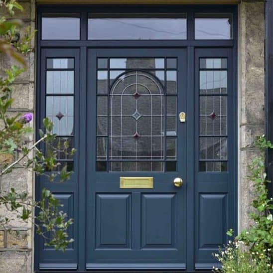 Large timber front door with leaded detailing, side panels, top light and brass letterbox, door knob and escutcheon