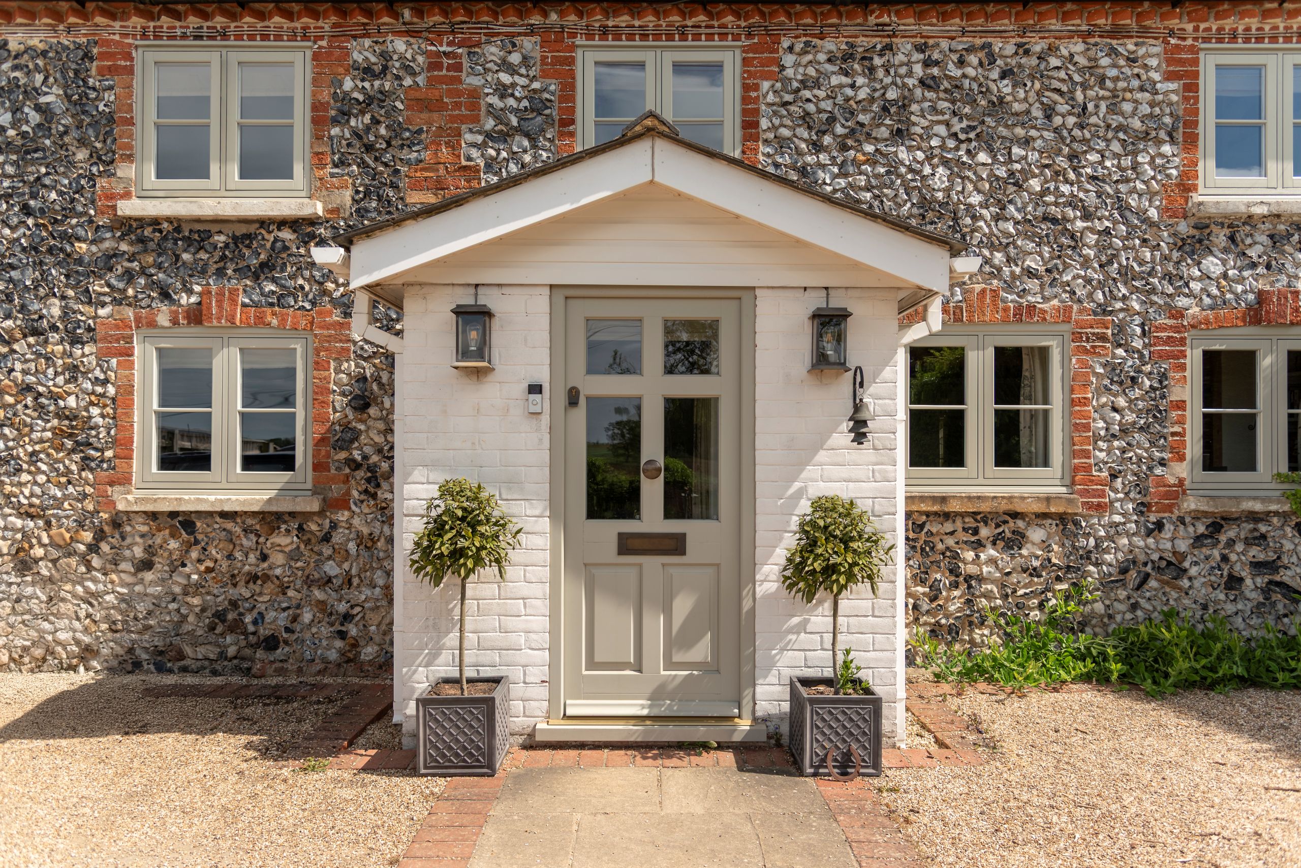 Engineered timber 'Frenchay' townhouse door with Samuel Heath antique brass unlacquered escutcheon, door knob and letterbox, in French Grey, with Evolution PVCu flush casement windows with a single horizontal Georgian bar in Olive Grey.