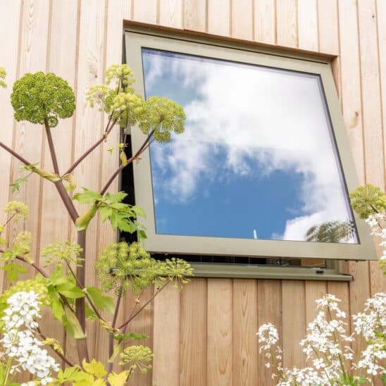 Slim framed, Olive Grey aluminium Sunflex bottom opening windows allow an uninterrupted view of the garden beyond.